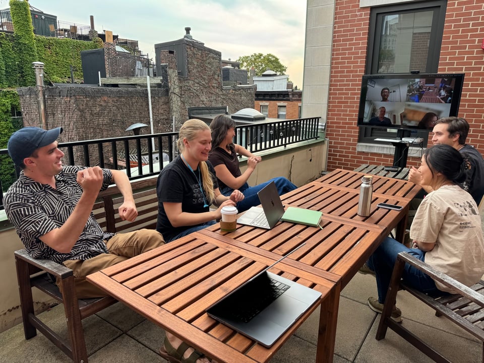 A group of people sitting around a long wooden table on a patio