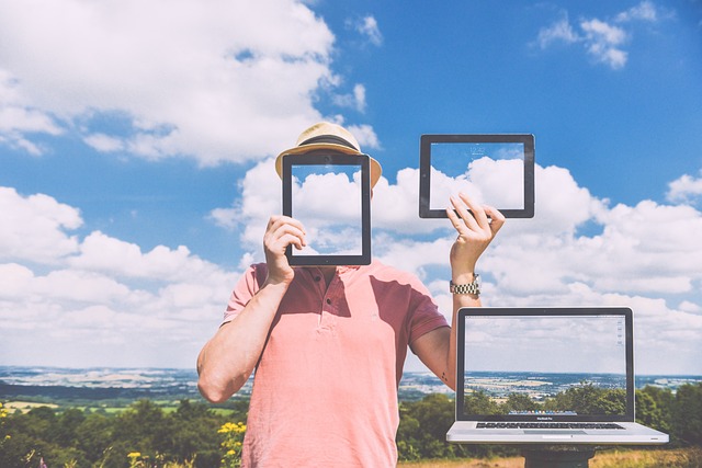 A person in a hat and a pink shirt holding an iPad against their face, which is reflecting the sky. They are holding another iPad reflecting the sky.