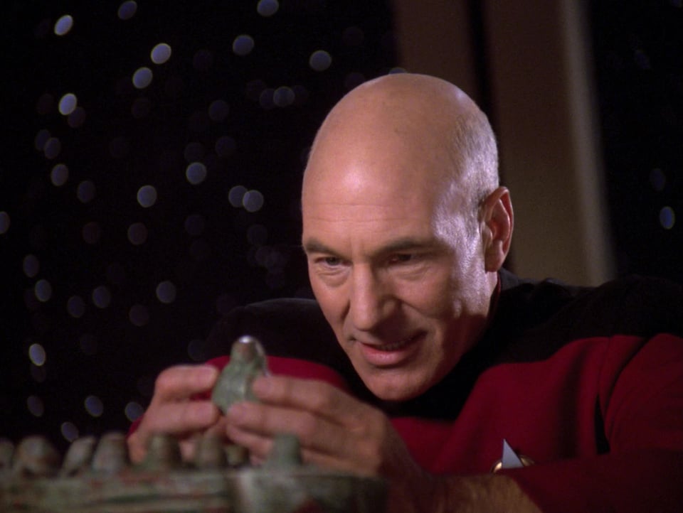 Captain Picard is carefully holding a small ceramic figure. He is focused and enthusiastic.