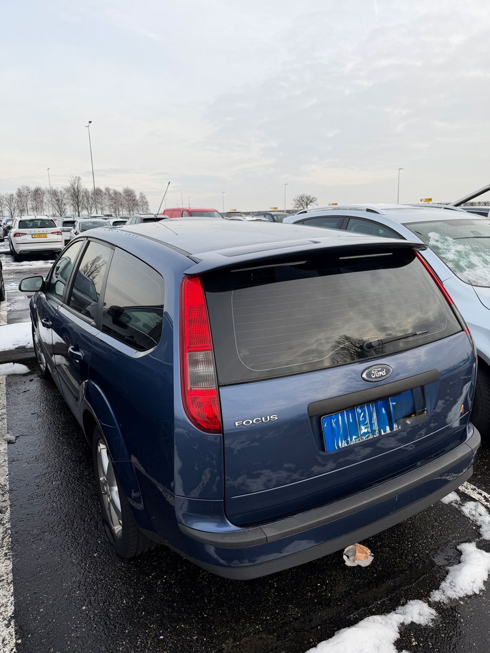 A car in a parking lot with some snow, but not too much surrounding it.