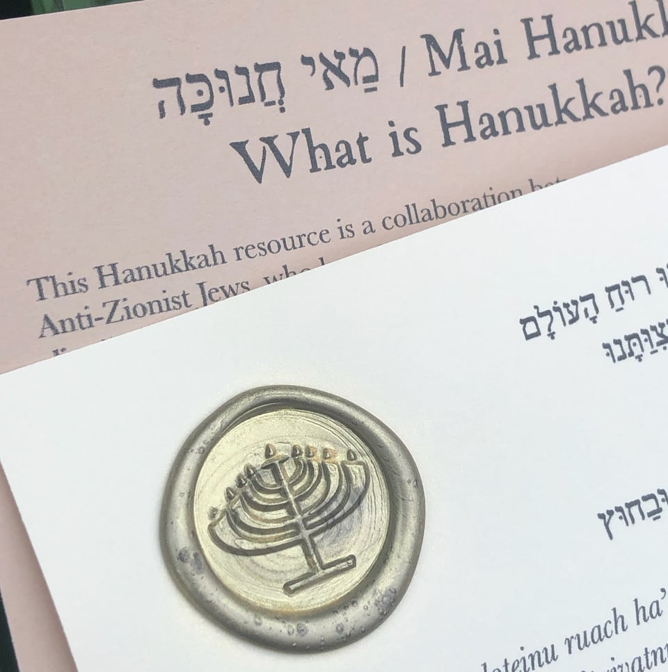 Image ID: A close-up photo of the Mai Hanukah resource. There are two pages, and the top page has a golden wax seal with the image of a round menorah.