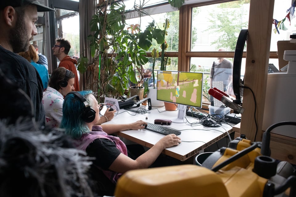 A group of people watch a bank of two screens lit up by a videogame.