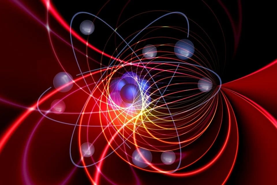 An atom with ghostly gray electrons orbiting around a fuzzy cloud of indeterminant nuclei. Red magnetic field lines cross in the background.