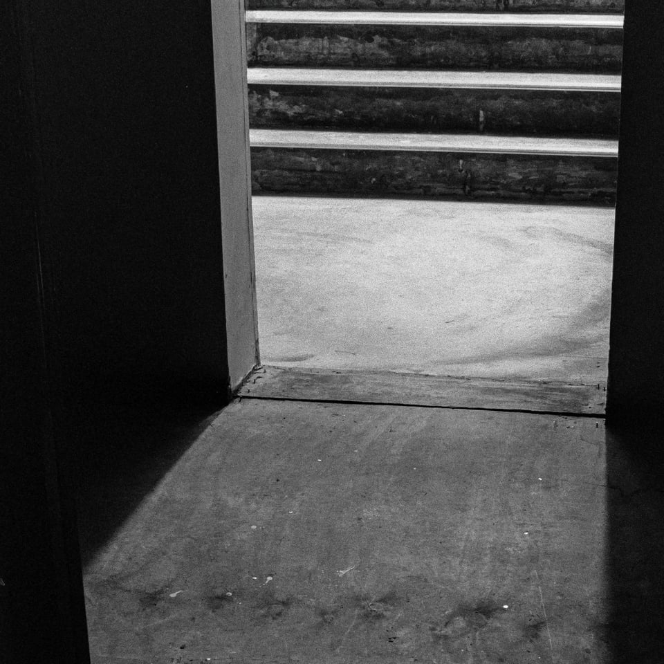 Album artwork for "It ends in a crypt." It is a black and white photograph taken from inside a doorway with stark shadows and stairs leading downward.