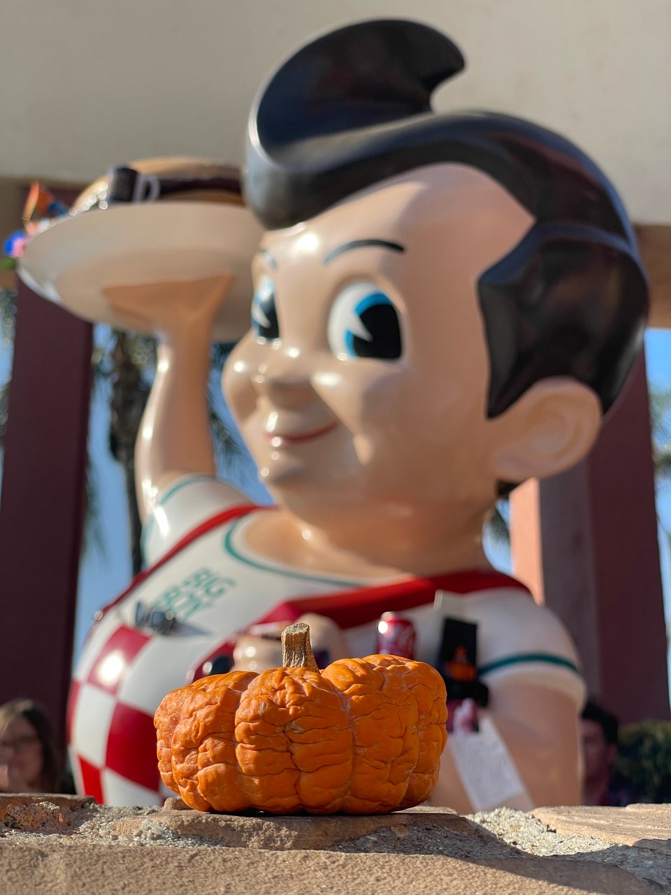 A large statue of a cartoon boy appears to stare at a rotting little pumpkin
