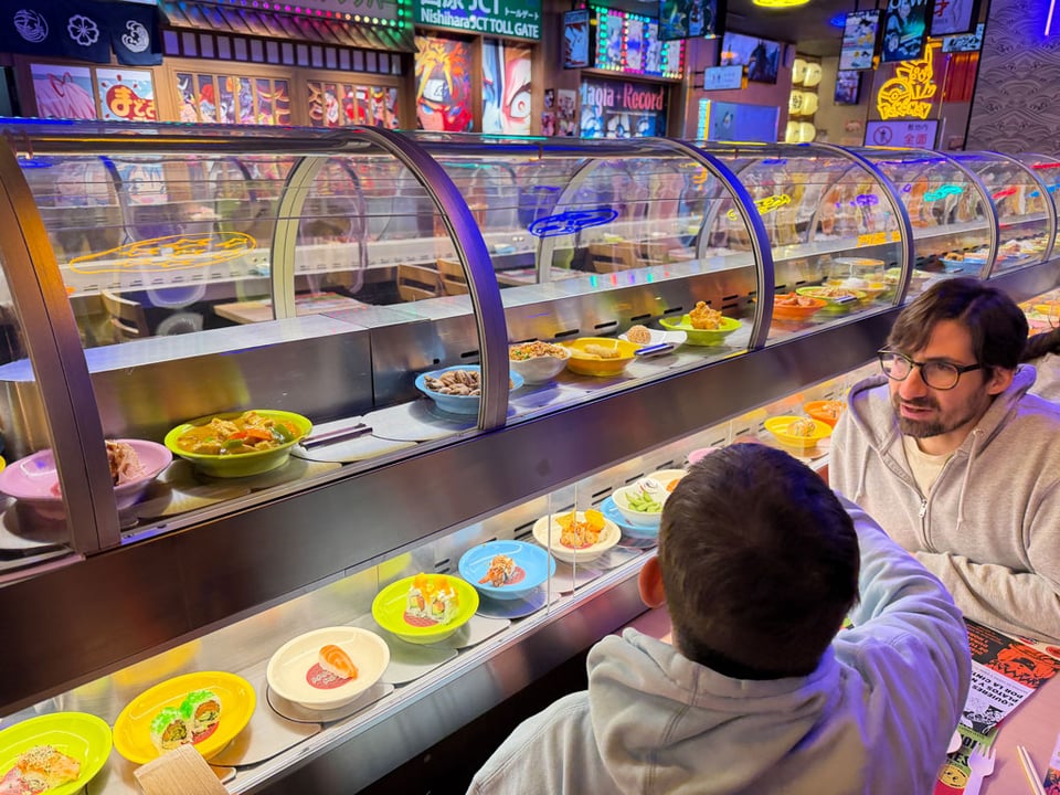 Two people look at the sushi rolling by on a 'treadmill' of food.