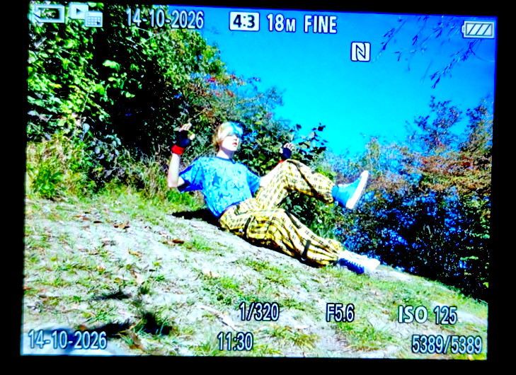 A photo of me making a falling pose on the ground on a hill.