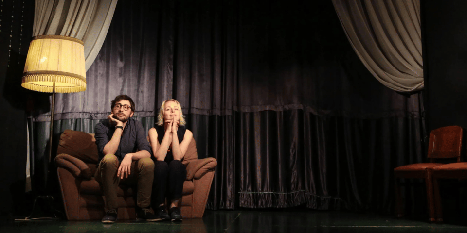 Gael and Laura sit on a stage with a lamp.