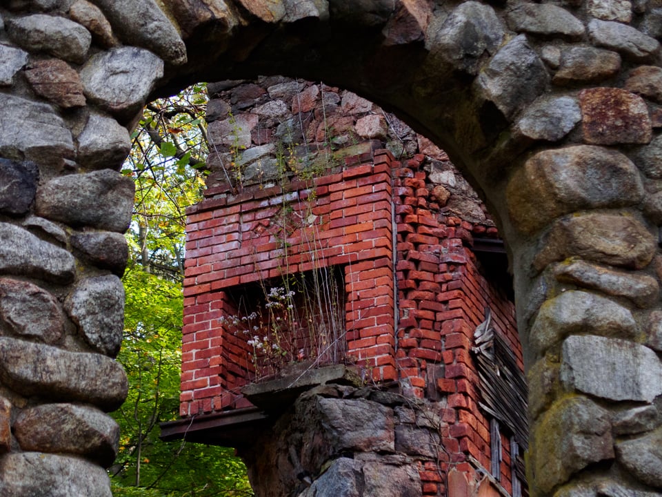 a red fireplace in a still standing chimney in a destroyed manor, still standing, with flowers growing in it, and visible through an arch.