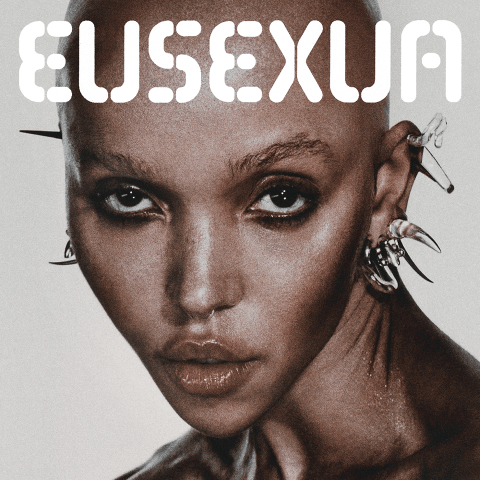 The album cover of FKA twigs' EUSEXUA. Her face looks at the camera devilishly, and she has a shaved head with many spikey glass earrings.