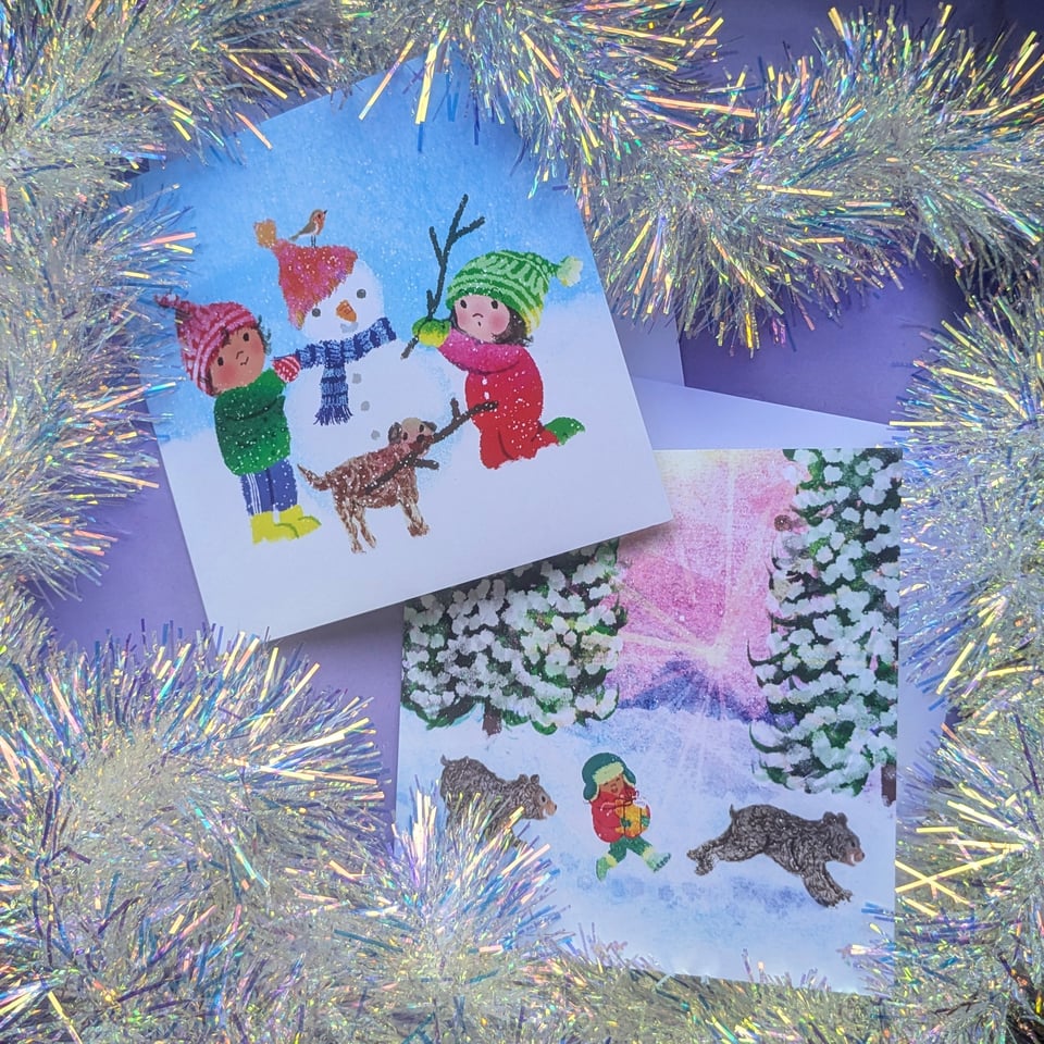 A photo of two festive cards by Kip Alizadeh surrounded by silver tinsel