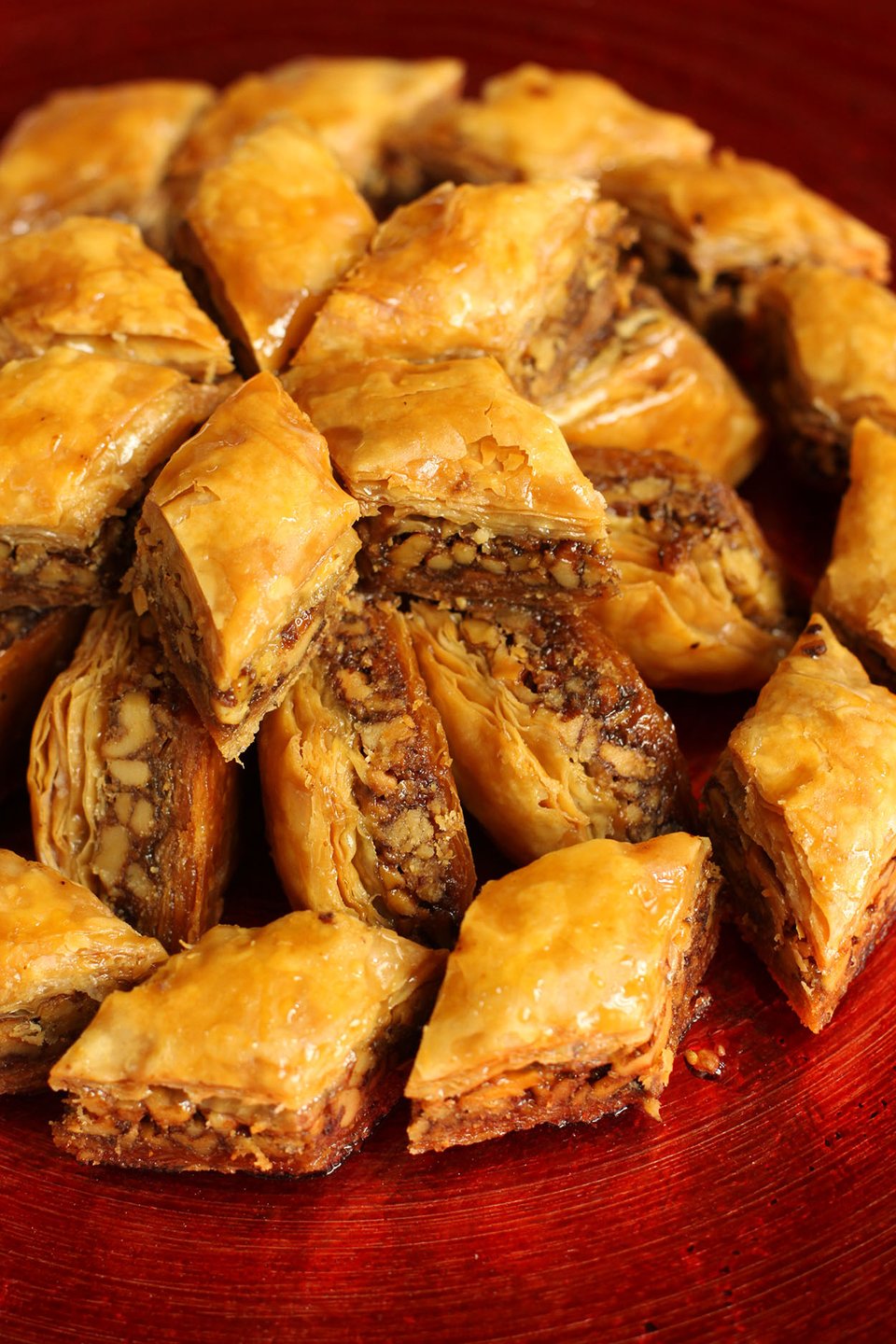 a photo of baklava stacked on a shiny red plate, copyright Adrianna Tan