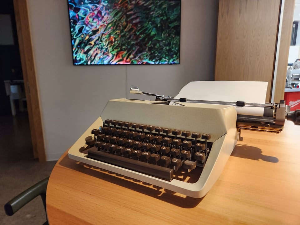 Kate's beige Facit typewriter on a table in front of a wall with a piece of luminescent abstract art.