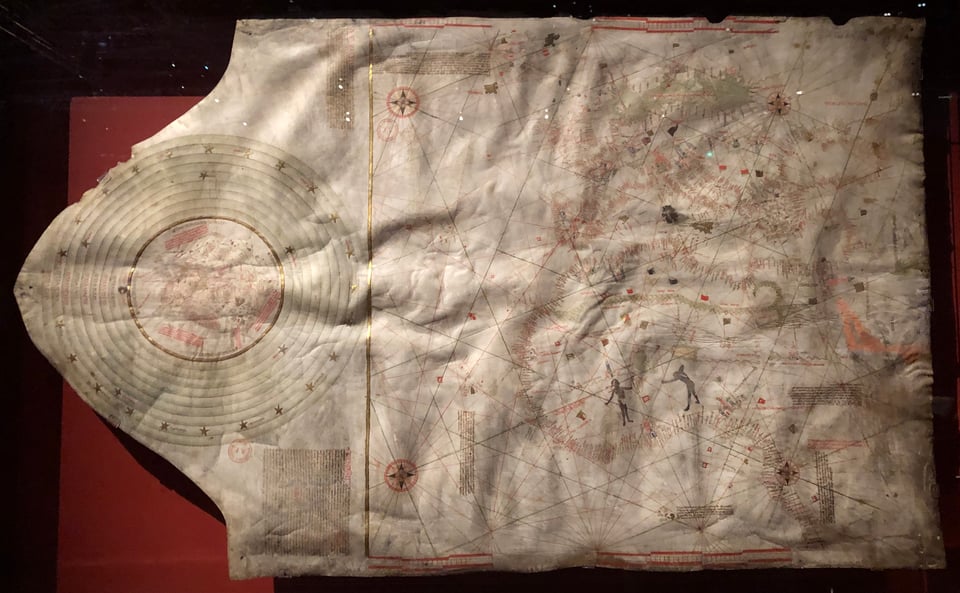 A horizontal medieval manuscript, roughly the shape of a rectangle with a triangle attached on the left, on which there’s a circular diagram. The rectangular part is a marine chart; the circular part a compressed world map surrounded by about nine concentric circles.