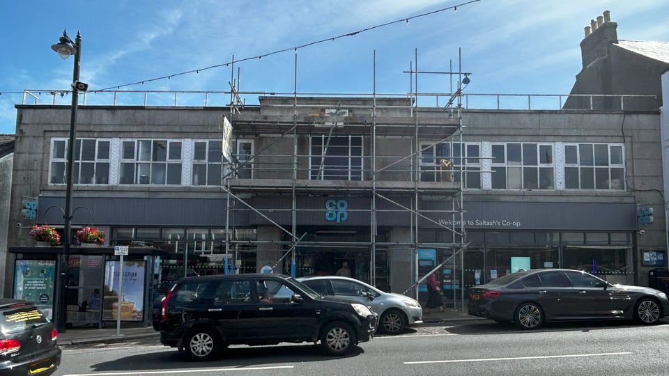 A 1930s shop, half hidden by scaffolding. At street level it's just a shop. Above it is the original 1930s elevation. It's symmetrical, with a central projecting entranceway with a vertical window. To either side, is a ribbon of windows.