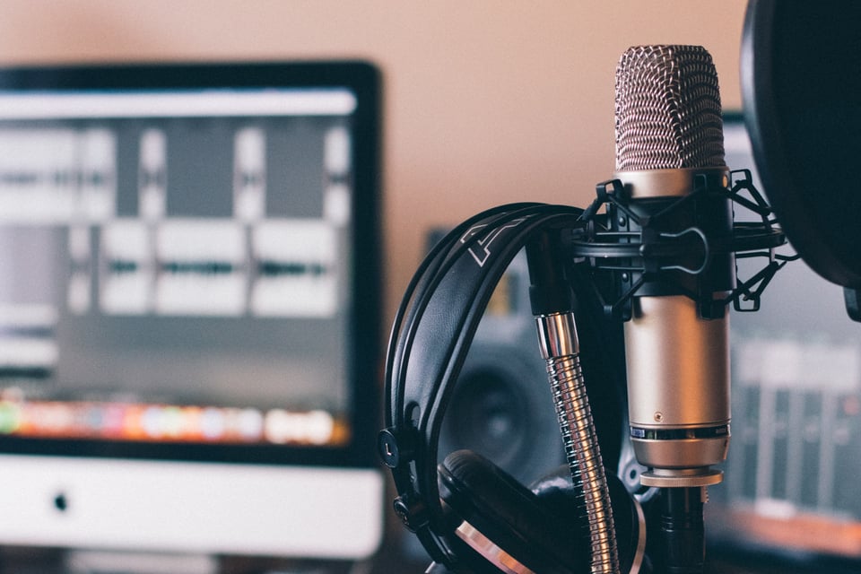 Description: Image of a microphone (in focus), with a computer screen in the background (blurry). Photo by Will Francis on Unsplash.