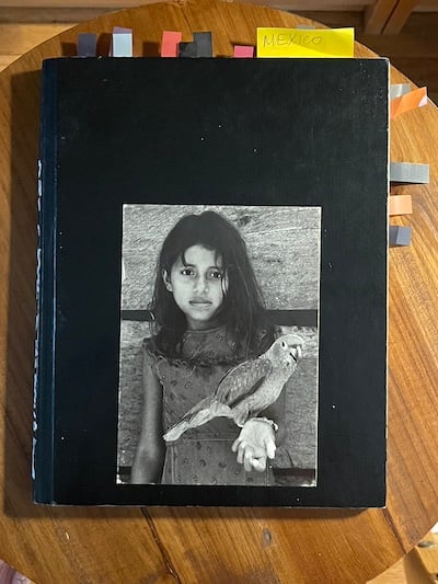 a black journal with a postcard glued to the front of a young brown girl holding her wrist out. A parrot stands on her wrist.