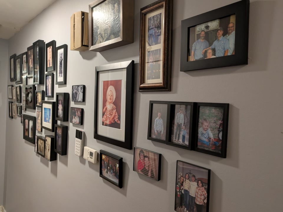 A hallway wall with several dozen family photos on it, displaying various generations.