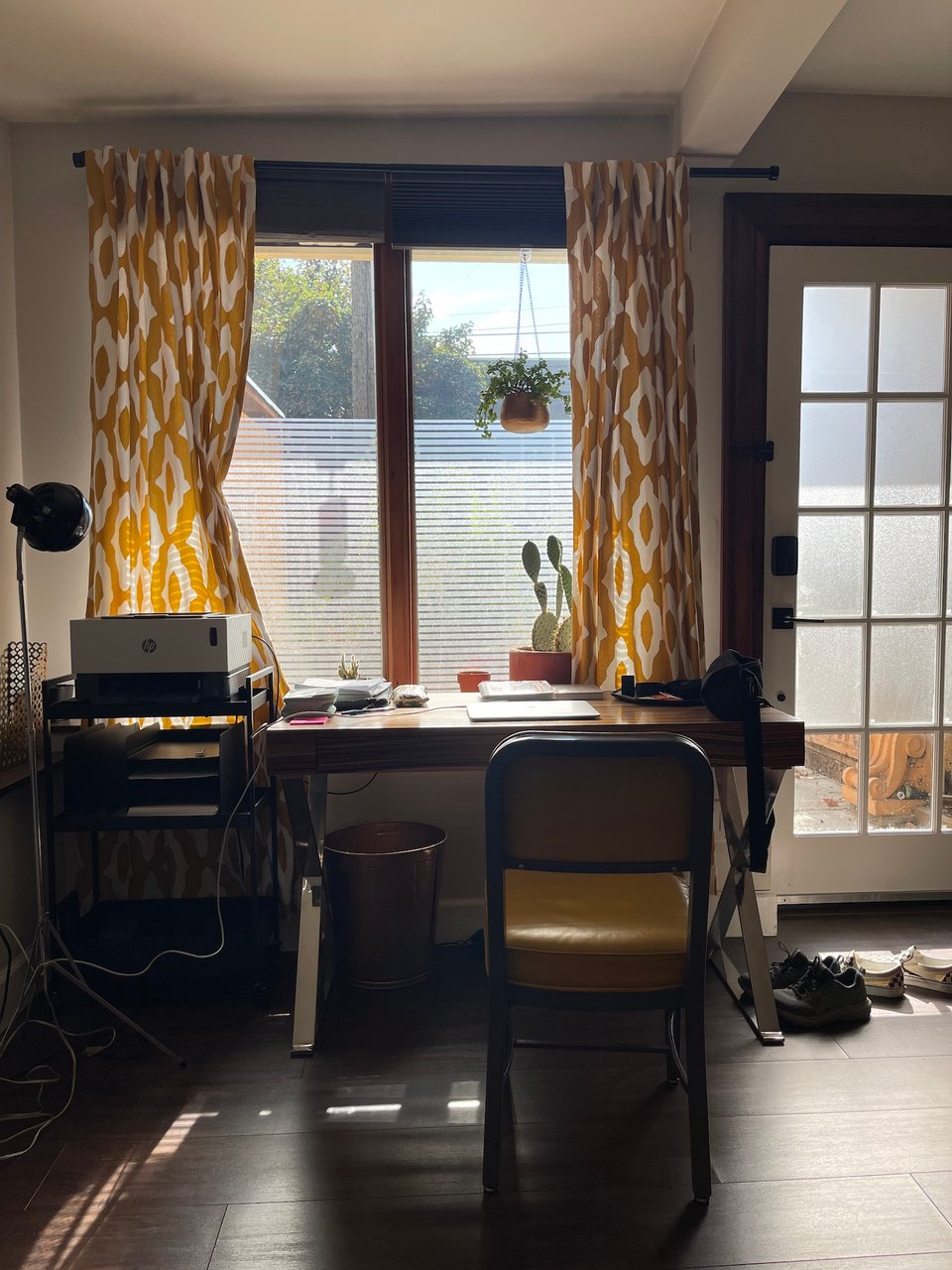 A view from inside one of the residences that the former Tin House/now McCormack Writing Center offer. A desk, chair, yellow and white pattern curtains, some shoes in front of the door, and a hanging plant.