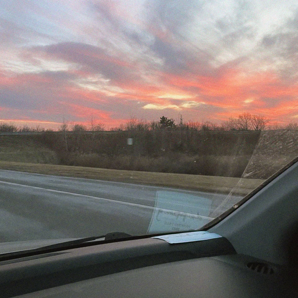 a beautiful hudson valley sunset seen from the confines of a car with a sun-faded rave parking pass in the window