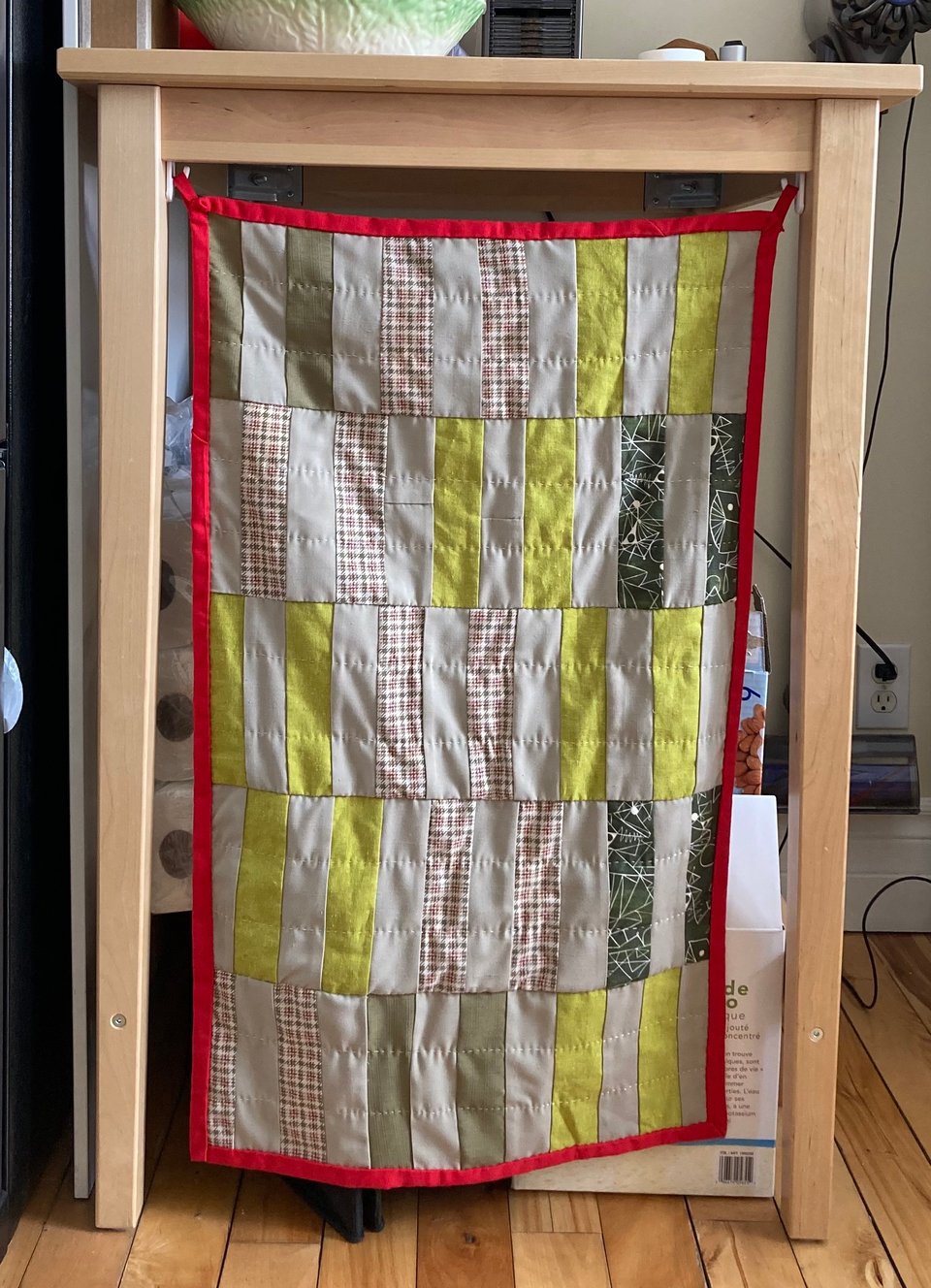 A green and beige quilt covering the area underneath a tall table in the kitchen