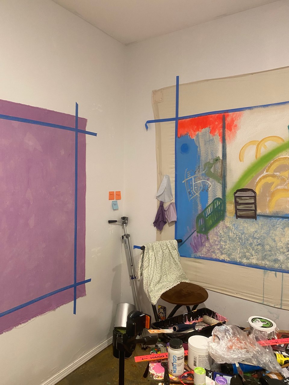 a corner of studio utopia with a blank purple canvas and a painting in progress