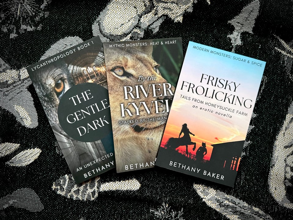 A photo of the paperback editions of The Gentle Dark: An Unexpected Werewolf, By the River Kyveli: Stalked by the Manticore, and Frisky Frolicking, Tails from Honeysuckle Farm