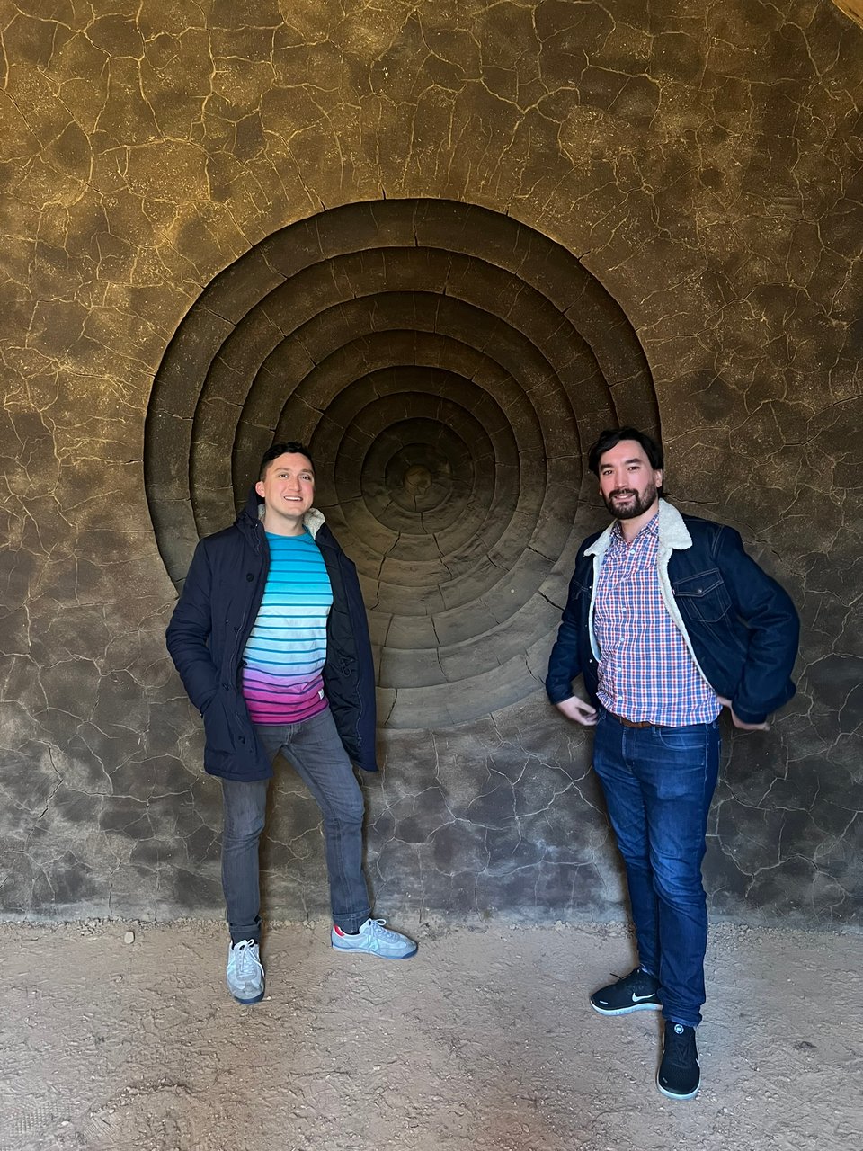 Two men, including the author, standing in front of a clay wall with concentric indentations