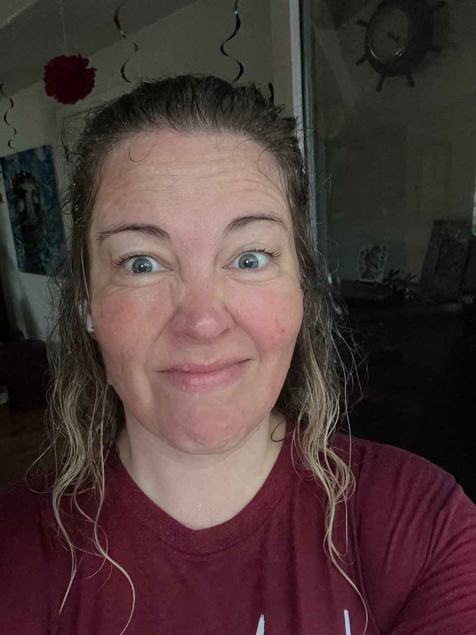 the author in a selfie, soaking wet with blond hair trailing down her face and neck, a water-dark red tee shirt, making a wincing smile.