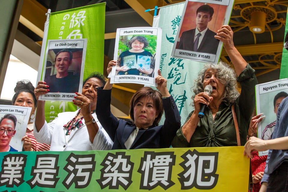 Three women hold up pictures of jailed Vietnamese activists, surrounded by green banners