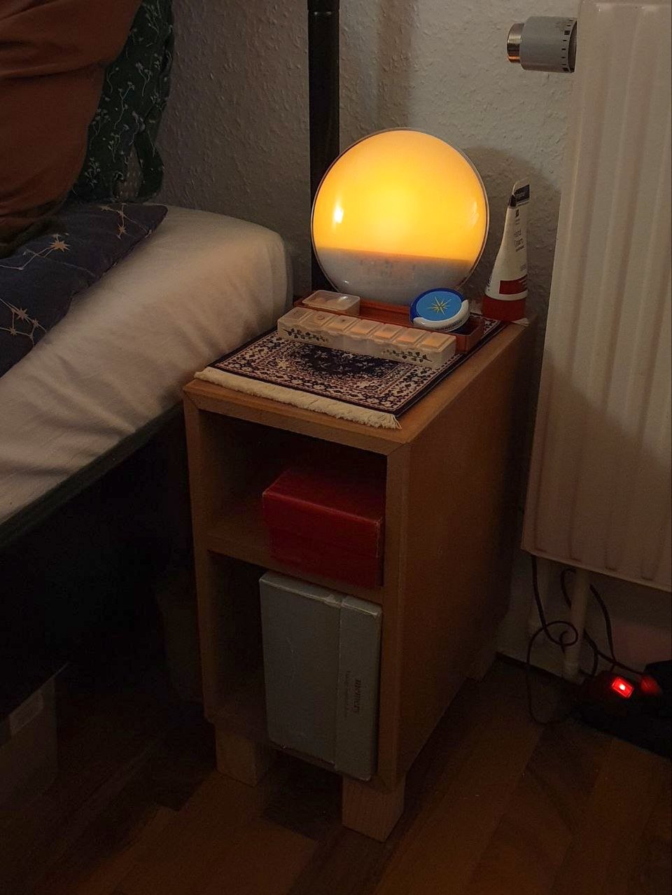 The nightstand with a nightlamp and other things on top and two open compartments, both holding boxes. The top compartment is bigger and holds a big green shoebox, however it is slotted in sideways. Apparently the material was too thick and I went by outside measurements so the box no longer fit.