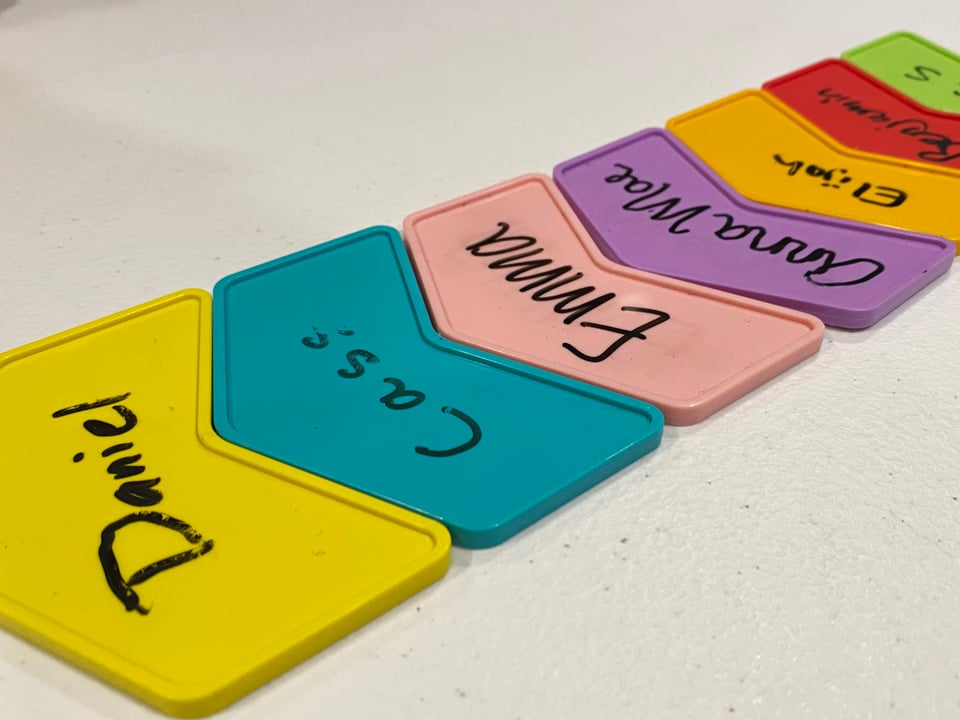 Chevron shaped plastic multi-colored tiles with people's names on them, arranged in a column