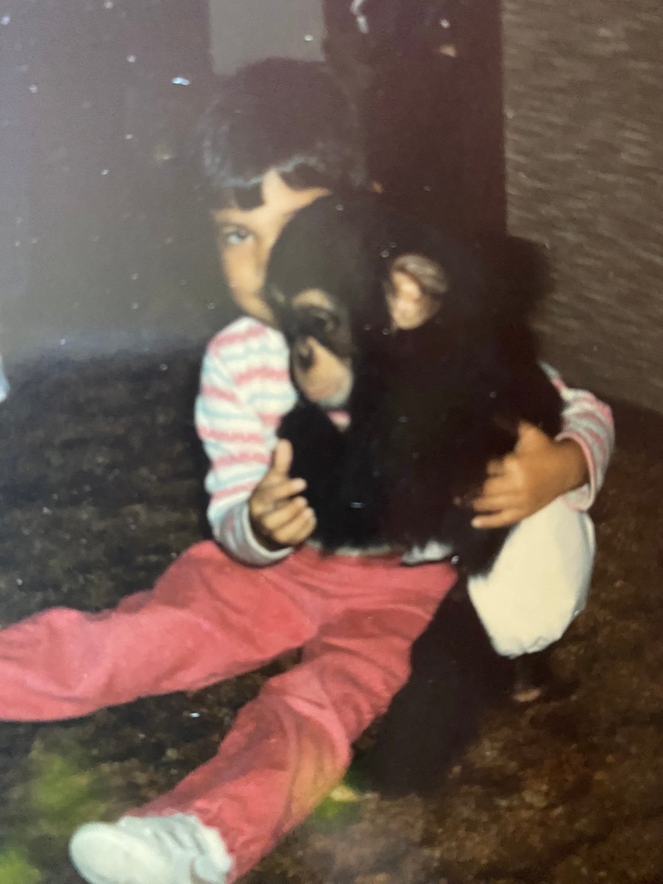 a young girl sits with legs outstretched holding a chimpanzee who is standing to her side