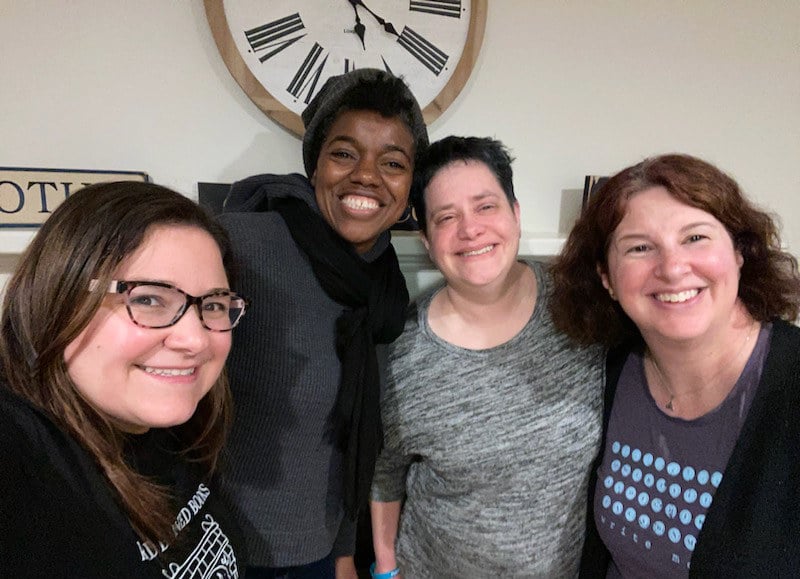 four women smiling in front of a clock