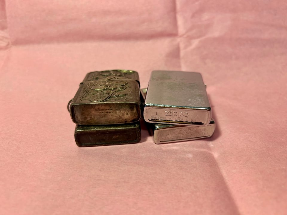 Four zippo lighters stacked up, sitting on pink paper.