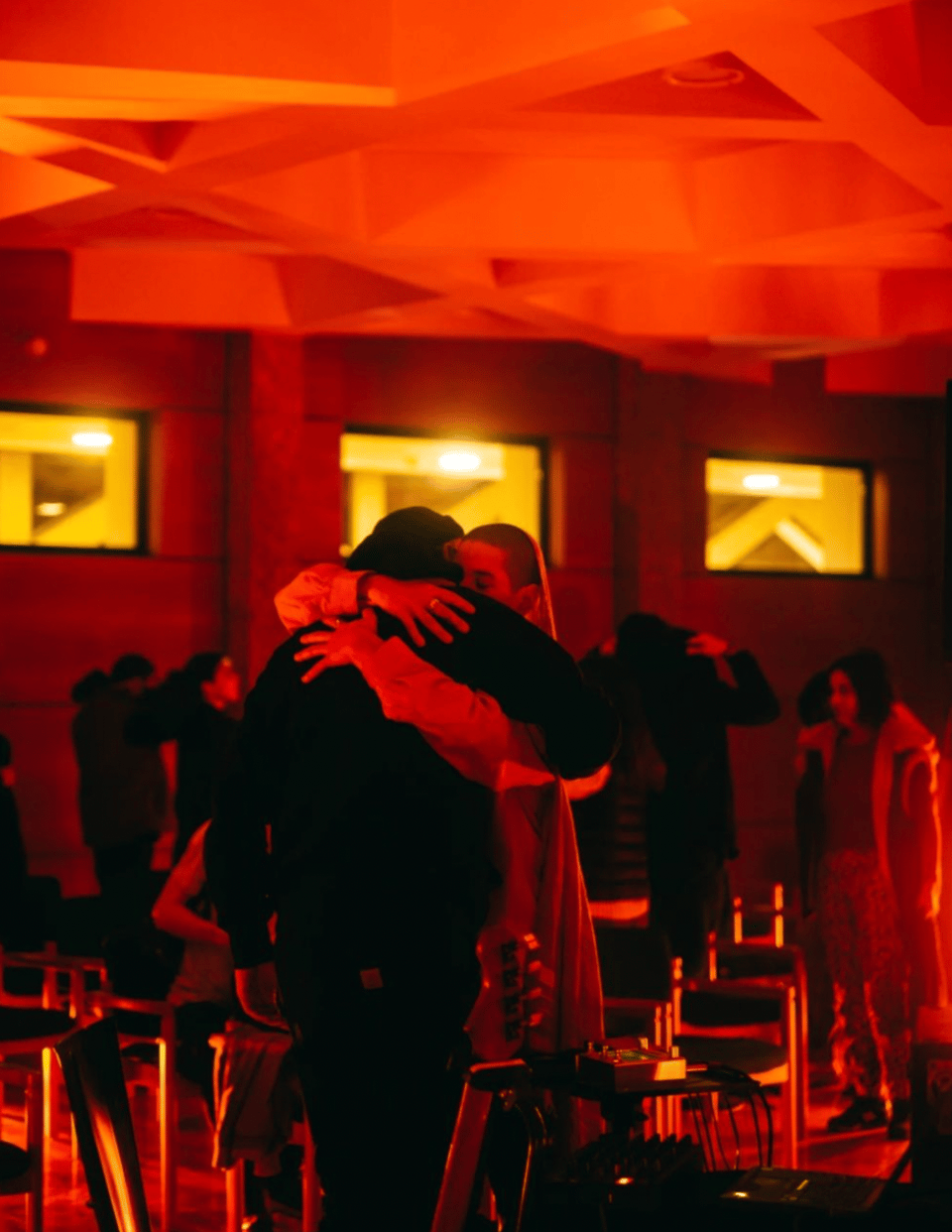 Dirar Kalash and ãssia ghendir, bathed in orange light, embrace as the audience leaves the room, under a ceiling patterned with six-pointed stars