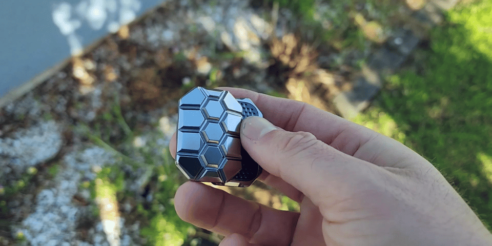 A shiny fidget slider made of metal with a honeycomb pattern.