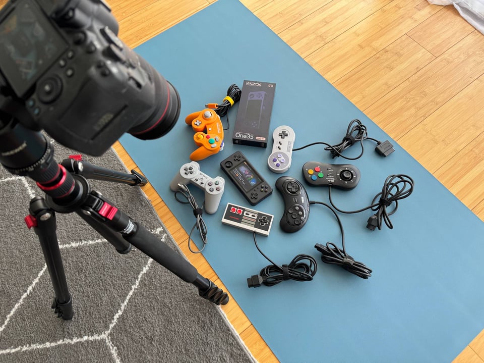 a camera pointing at a blue floormat with a retro gaming handheld surrounded by game controllers