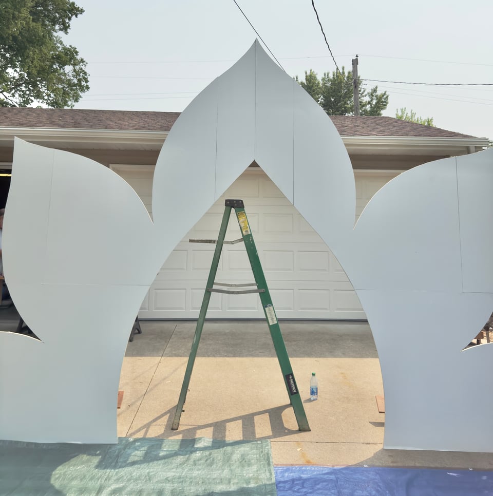 White arch display standing on driveway with ladder standing behind it.