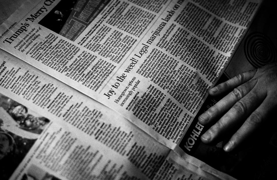 A black-and-white image of an open newspaper. On the right-hand side, a hand touches the pages. Photo by Hayden Walker on Unsplash.