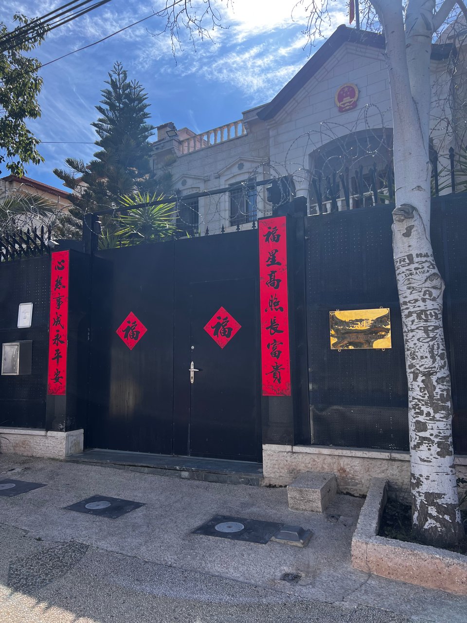 A building with a black gate in front, that includes red vertical banners with Chinese writing