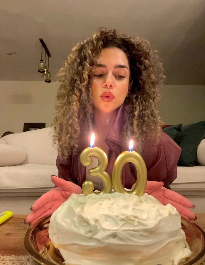 A woman with beautiful long curly hair blowing out two candles (3-0) on a birthday cake