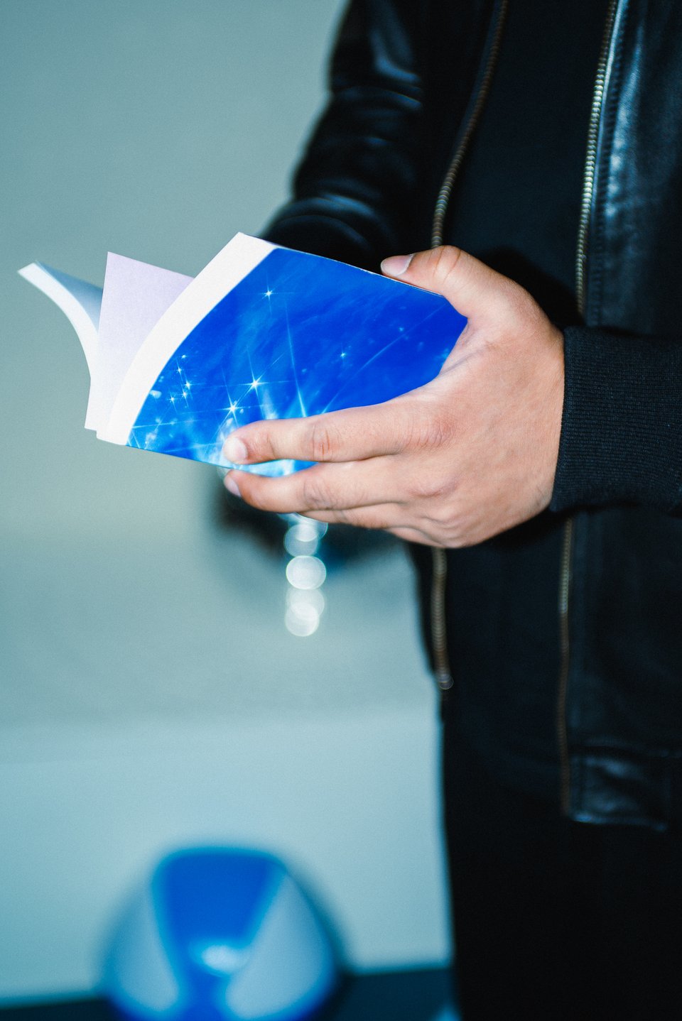 A close up of a hand holding the blue book with a blue and white beach ball seen in the background.