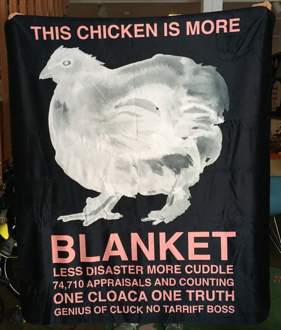 An idiot holding up an even stupider blanket with a painting of a chicken that says: THIS CHICKEN IS MORE BLANKET LESS DISASTER MORE CUDDLE 74,710 APPRAISALS AND COUNTING ONE CLOACA ONE TRUTH GENIUS OF CLUCK NO TARRIFF BOSS