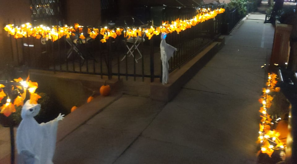 Night time photograph looking down a sidewalk with the key feature being a string of orange leaf-shaped lights covering the rail of a short residential cast-iron fence.
