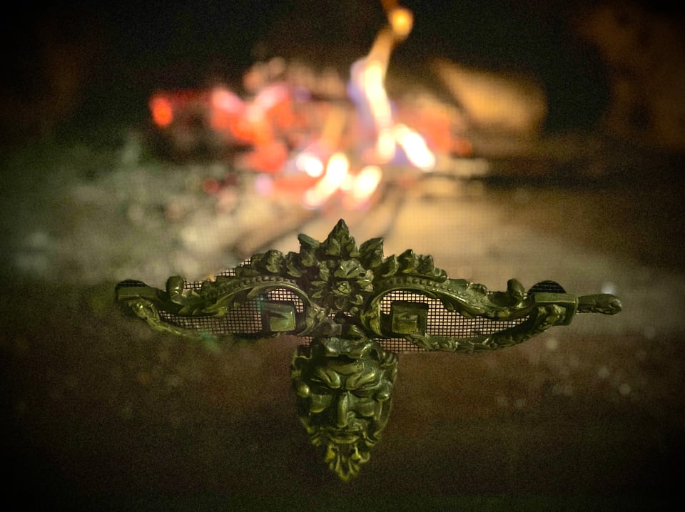 A fire screen with a metal decoration of a bearded face is in focus, the fire behind is out of focus.