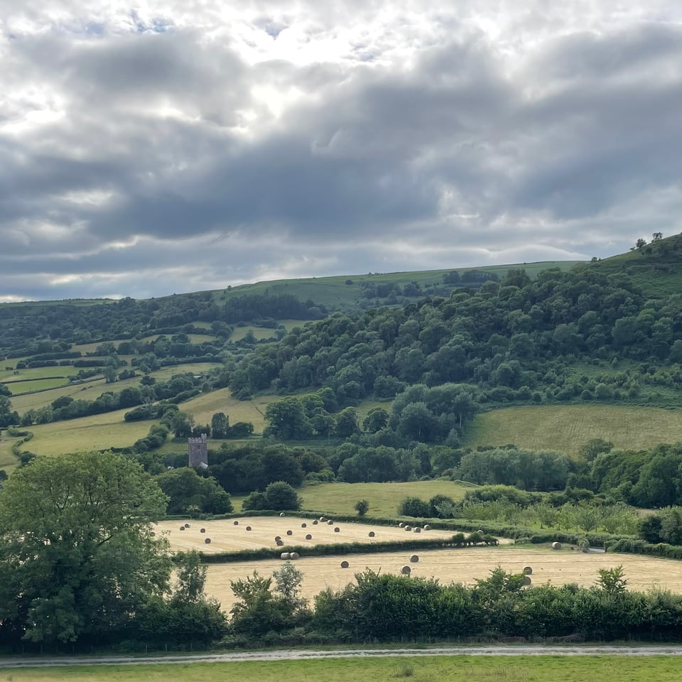 A view of fields with hay bales and St. Michael and All Angels Church in the distance
