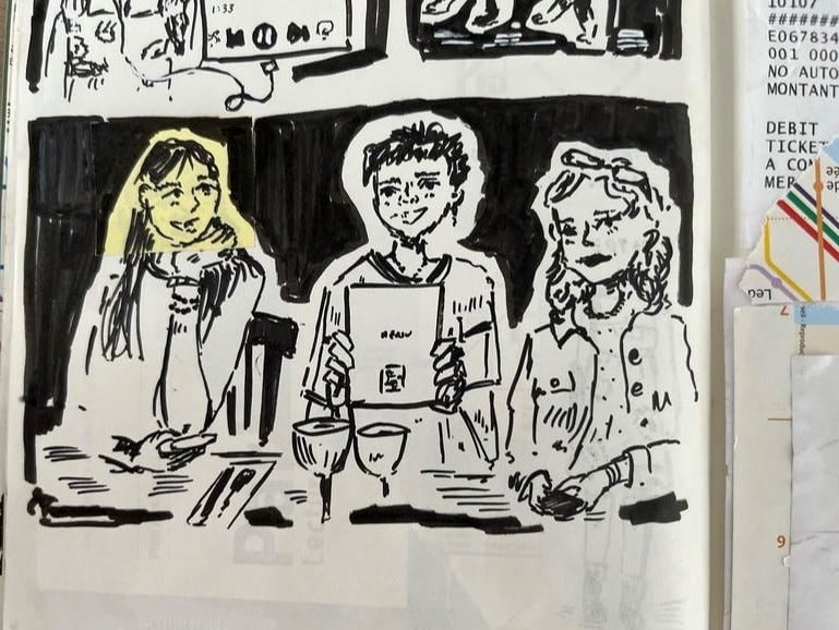 A close up from a page in Q's sketchbook displayed at the showcase for her Paris College of Art exhibition that includes a drawing of 3 people at a cafe, with Q on the left, smiling, her head glowing yellow because made from a post it.
