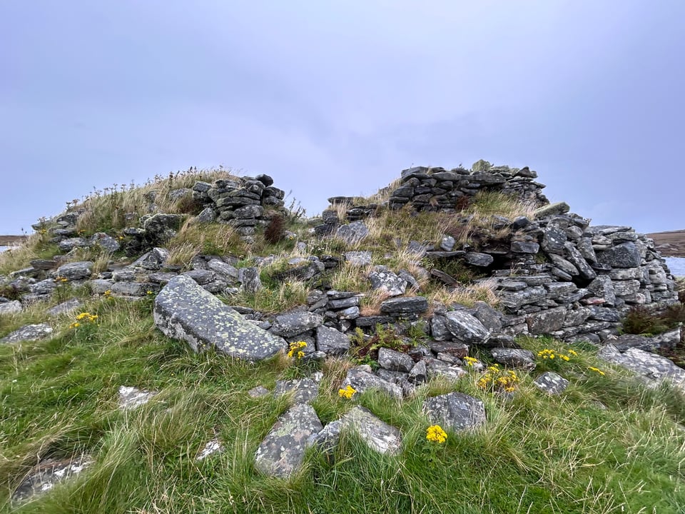A close-up of Dun an Sticir, a dilapidated broch overgrown with grass and wildflowers on an island in a loch on North Uist.