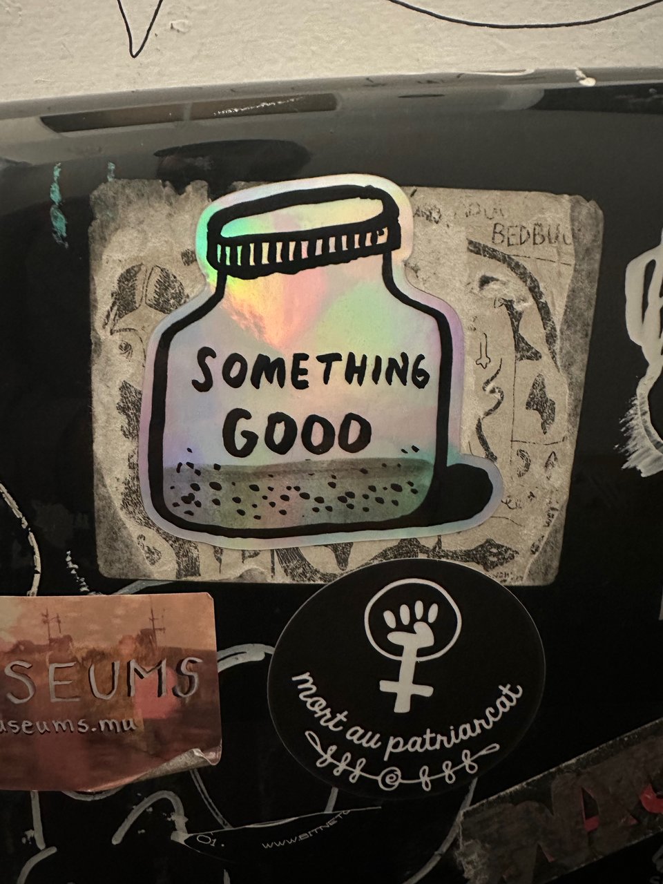 A Something Good sticker on a toilet paper dispenser in a toilet stall in a bar.